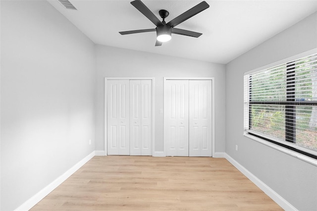 unfurnished bedroom featuring lofted ceiling, two closets, light wood-style flooring, baseboards, and ceiling fan