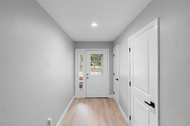 doorway with light wood-style flooring, baseboards, a textured wall, and recessed lighting