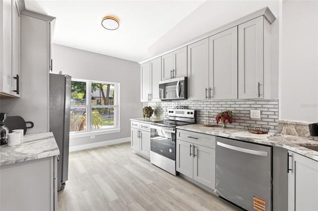 1738 Palm Rd, Ormond Beach, FL 32174 - kitchen with appliances with stainless steel finishes, backsplash, gray cabinetry, light wood-style flooring, and light stone countertops