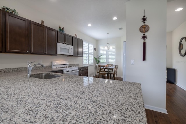 kitchen featuring white appliances, a sink, light stone countertops, dark brown cabinetry, and dark wood finished floors