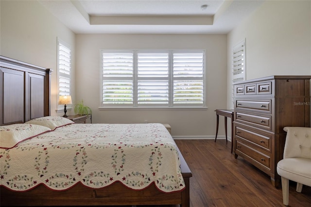bedroom featuring dark wood-type flooring, a raised ceiling, and baseboards