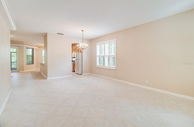 empty room with a chandelier, light tile patterned floors, healthy amount of natural light, and baseboards