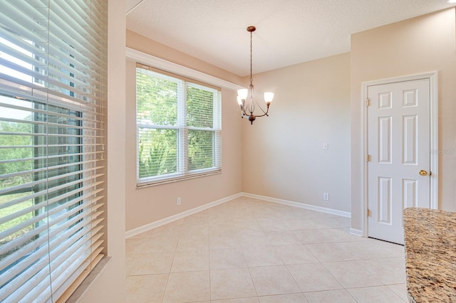 empty room featuring a chandelier, light tile patterned flooring, and baseboards