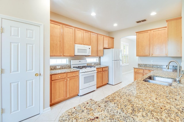 kitchen featuring white appliances, a sink, light tile patterned floors, arched walkways, and light stone countertops