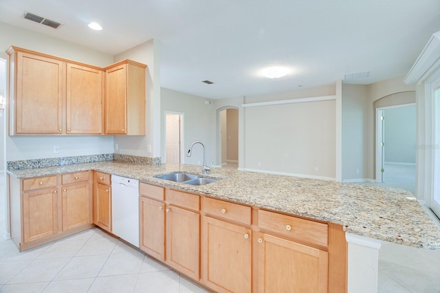 kitchen featuring white dishwasher, light brown cabinetry, a sink, arched walkways, and light tile patterned floors