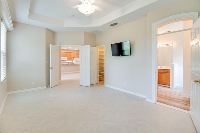 unfurnished bedroom featuring a tray ceiling, freestanding refrigerator, a spacious closet, baseboards, and light tile patterned floors