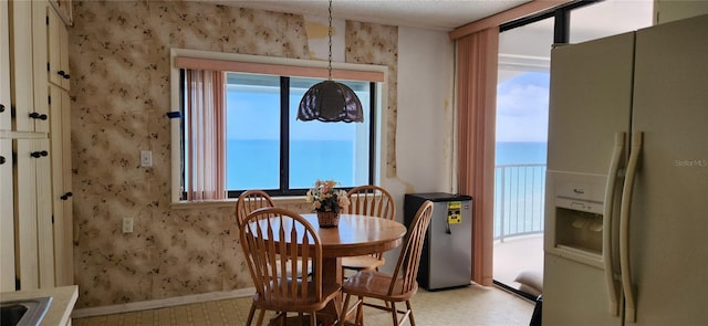 dining space featuring wallpapered walls, light floors, and baseboards