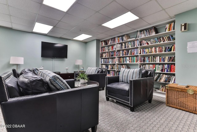 carpeted home office featuring a paneled ceiling, built in features, and wall of books