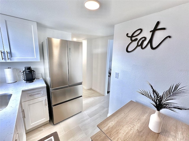 3112 S Atlantic Ave, Daytona Beach, FL 32118 - kitchen featuring freestanding refrigerator, white cabinets, a textured wall, light tile patterned flooring, and light stone counters