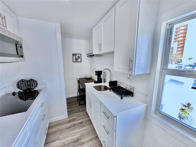3112 S Atlantic Ave, Daytona Beach, FL 32118 - kitchen with stainless steel microwave, a sink, light wood-style floors, white cabinets, and black electric cooktop