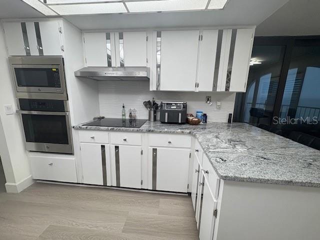 kitchen featuring stainless steel appliances, wall chimney exhaust hood, white cabinetry, light stone counters, and baseboards