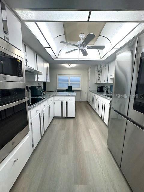 kitchen with appliances with stainless steel finishes, light wood-style floors, a peninsula, a ceiling fan, and light countertops