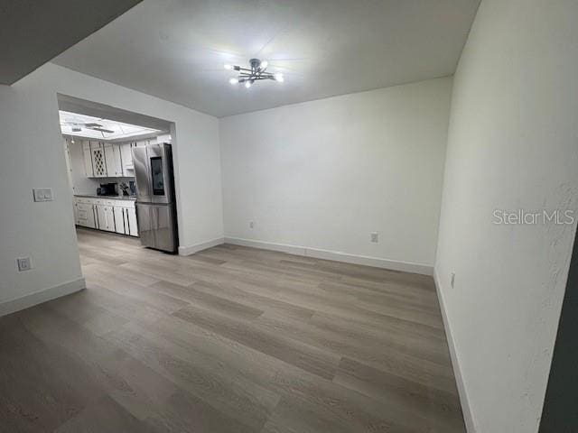 unfurnished living room featuring baseboards, light wood-type flooring, and a chandelier