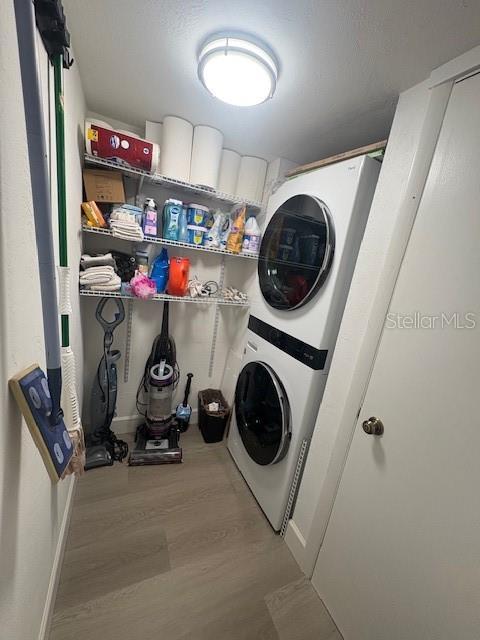 laundry room featuring stacked washer / drying machine, wood finished floors, and baseboards