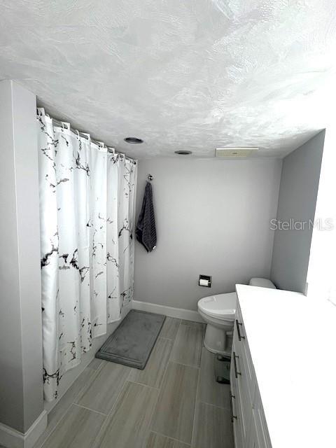 bathroom featuring baseboards, toilet, a shower with curtain, and vanity