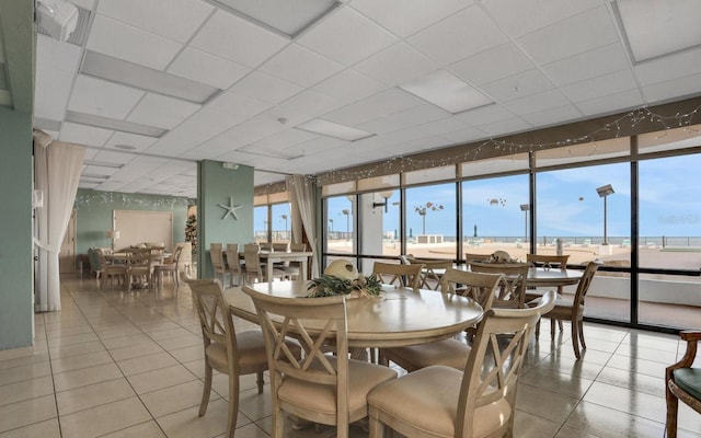dining room with light tile patterned flooring, a wall of windows, and a drop ceiling