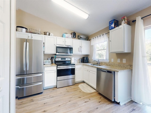2978 Greynolds St, Deltona, FL 32738 - kitchen with stainless steel appliances, light wood-style flooring, white cabinetry, vaulted ceiling, and light stone counters
