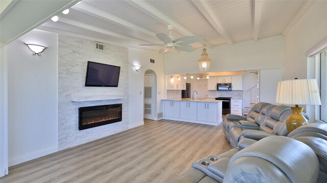 8 Ocean Dunes Dr, Ormond Beach, FL 32176 - living area featuring light wood-style floors, beam ceiling, a stone fireplace, a ceiling fan, and arched walkways
