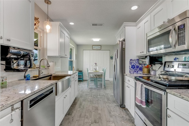 114 Ocean Aire Ter N, Ormond Beach, FL 32176 - kitchen featuring stainless steel appliances, white cabinetry, light wood-style floors, light stone counters, and decorative light fixtures