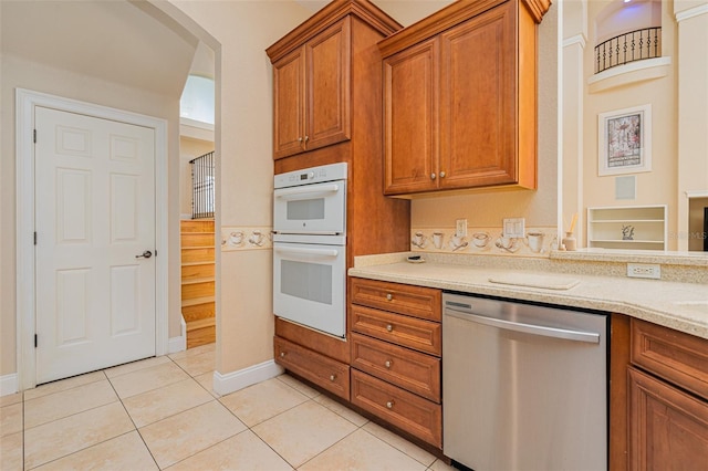 4427 S Atlantic Ave, Port Orange, FL 32127 - kitchen featuring dishwasher, white double oven, brown cabinets, light tile patterned floors, and baseboards
