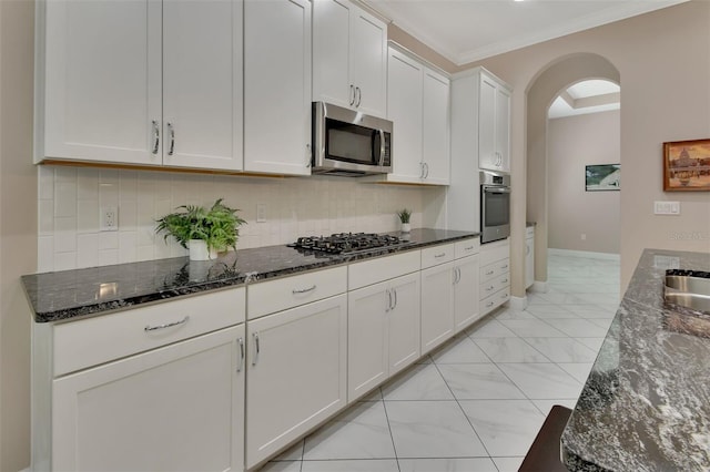 171 Birchmont Dr, Deland, FL 32724 - kitchen with appliances with stainless steel finishes, arched walkways, dark stone countertops, white cabinetry, and decorative backsplash