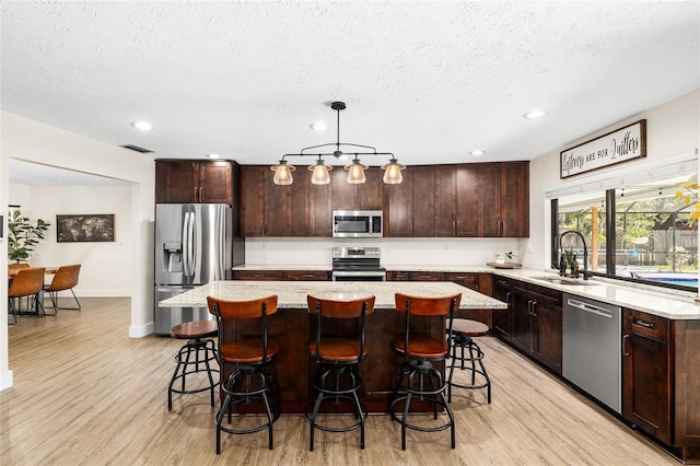 4301 Hudson Ln, Tampa, FL 33618 - kitchen with appliances with stainless steel finishes, a sink, light wood-style floors, a textured ceiling, and a center island