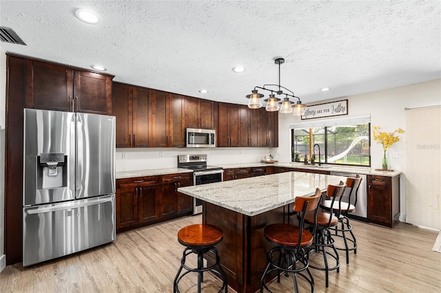 4301 Hudson Ln, Tampa, FL 33618 - kitchen with appliances with stainless steel finishes, light wood-type flooring, a textured ceiling, light stone countertops, and a breakfast bar area