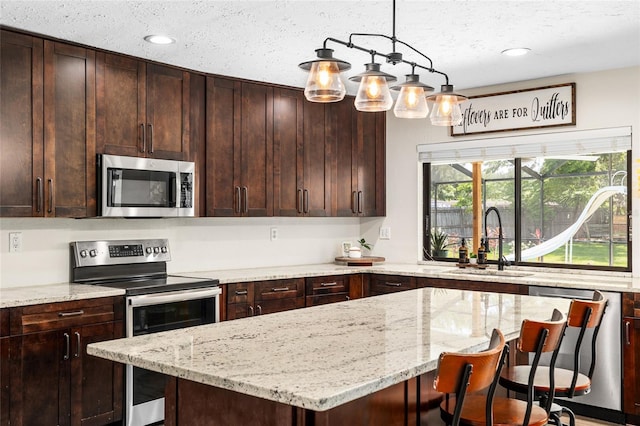 4301 Hudson Ln, Tampa, FL 33618 - kitchen featuring appliances with stainless steel finishes, a sink, a center island, light stone countertops, and a breakfast bar area