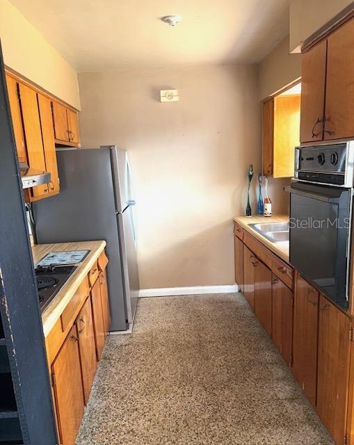 3 Cassia Ln, Debary, FL 32713 - kitchen with oven, baseboards, brown cabinetry, freestanding refrigerator, and a sink