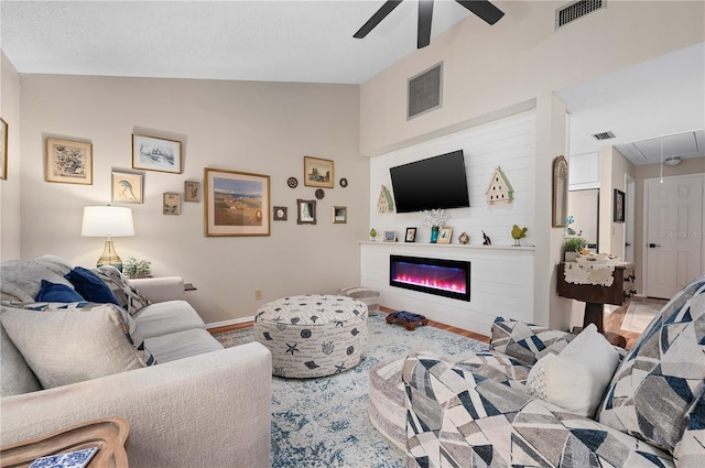 living room featuring attic access, ceiling fan, vaulted ceiling, a glass covered fireplace, and baseboards
