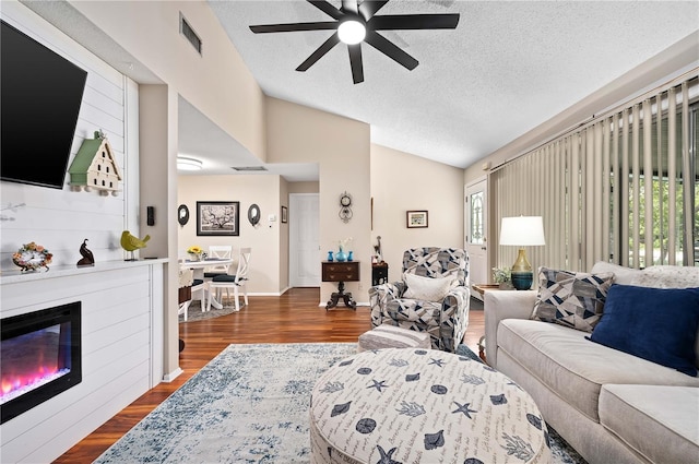 living room featuring vaulted ceiling, a ceiling fan, wood finished floors, a textured ceiling, and a fireplace
