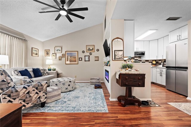 living room with ceiling fan, vaulted ceiling, wood finished floors, a textured ceiling, and a glass covered fireplace