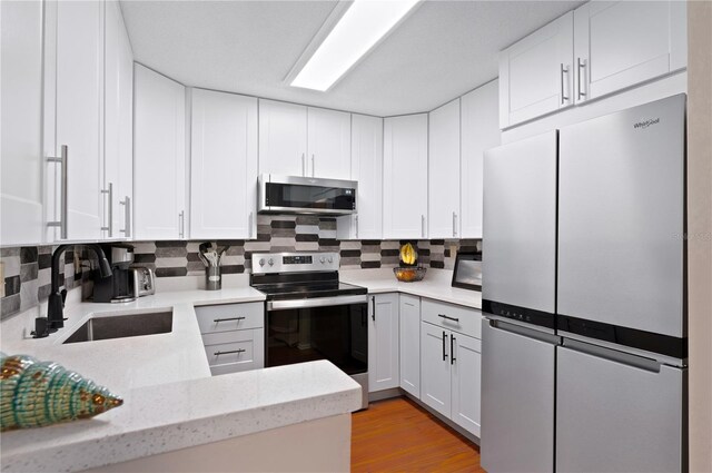 kitchen with stainless steel appliances, a sink, backsplash, and white cabinetry
