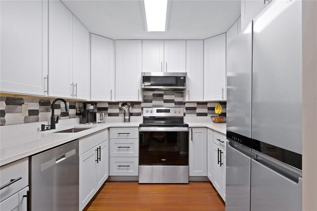 kitchen with stainless steel appliances, a sink, light countertops, tasteful backsplash, and white cabinetry