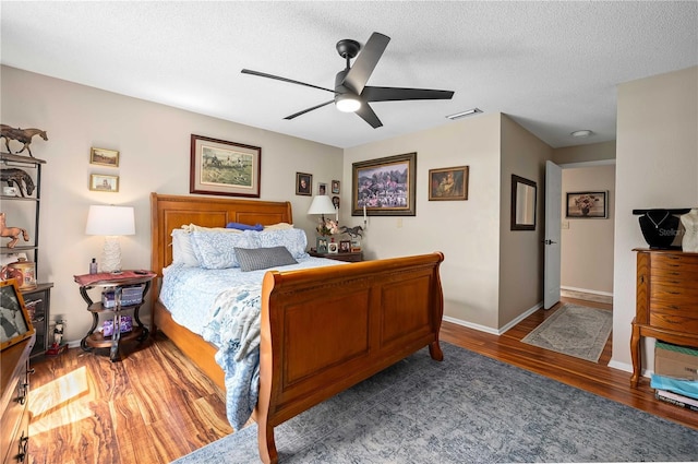 bedroom with wood finished floors, a ceiling fan, baseboards, and a textured ceiling