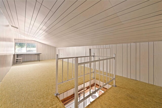 hall with carpet, vaulted ceiling, and wooden walls