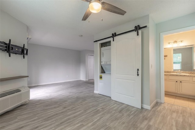 1401 S Palmetto Ave Unit 119, Daytona Beach, FL 32114 - unfurnished living room featuring stacked washer / dryer, a barn door, a ceiling fan, light wood-style floors, and baseboards
