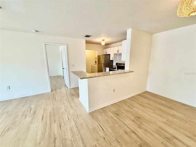 940 Village Trl Unit 8-205, Port Orange, FL 32127 - kitchen with freestanding refrigerator, light wood finished floors, white cabinetry, light stone countertops, and open floor plan