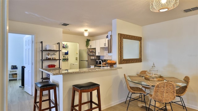 940 Village Trl Unit 8-205, Port Orange, FL 32127 - kitchen with freestanding refrigerator, light wood-style floors, white cabinets, a peninsula, and light stone counters