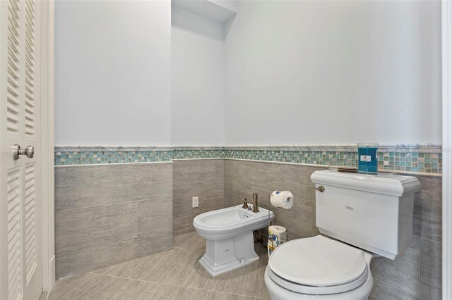 2275 Genesea Ln, Vero Beach, FL 32963 - bathroom with a bidet, tile patterned floors, tile walls, toilet, and a wainscoted wall
