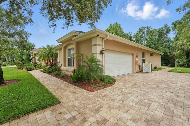 33 Coquina Ridge Way, Ormond Beach, FL 32174 - view of property exterior with stucco siding, an attached garage, decorative driveway, central AC, and a lawn
