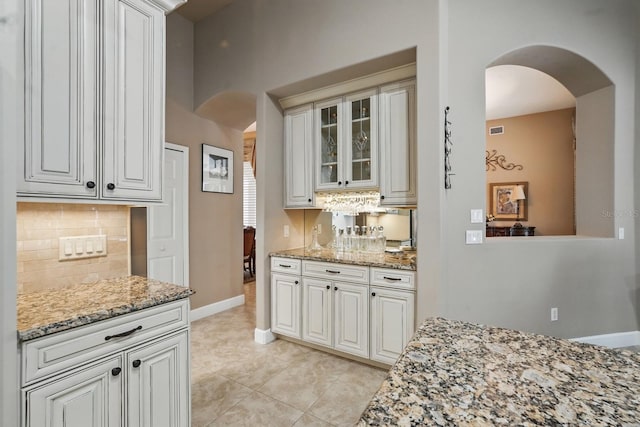 33 Coquina Ridge Way, Ormond Beach, FL 32174 - kitchen with arched walkways, tasteful backsplash, light stone counters, glass insert cabinets, and light tile patterned floors