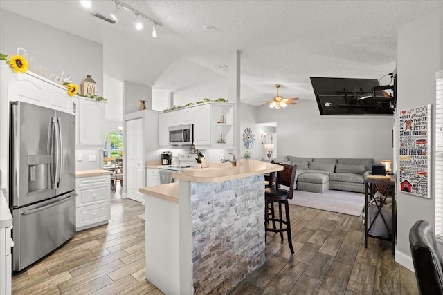 3132 Mango Tree Dr, Edgewater, FL 32141 - kitchen with stainless steel appliances, a kitchen bar, white cabinetry, wood finished floors, and a textured ceiling