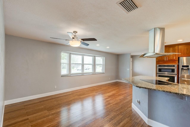 65 Sycamore Cir, Ormond Beach, FL 32174 - kitchen featuring island exhaust hood, stainless steel appliances, brown cabinets, a ceiling fan, and light wood-style flooring