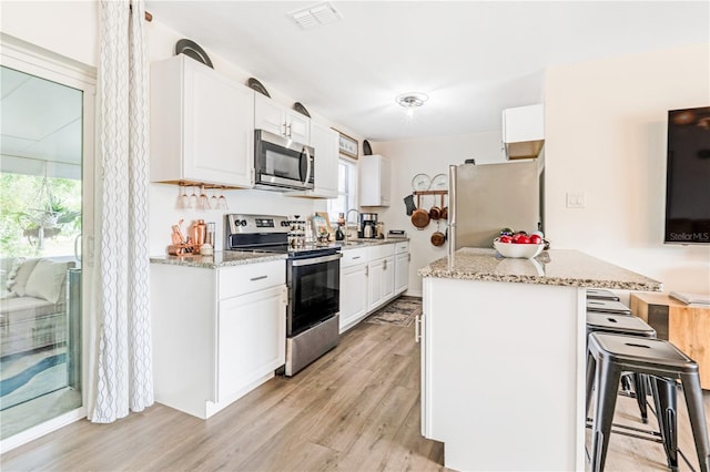 1455 Whitewood Dr, Deltona, FL 32725 - kitchen with stainless steel appliances, a breakfast bar area, light wood finished floors, white cabinetry, and light stone countertops