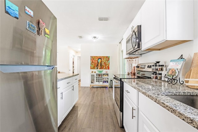 1455 Whitewood Dr, Deltona, FL 32725 - kitchen featuring appliances with stainless steel finishes, wood finished floors, light stone countertops, and white cabinets