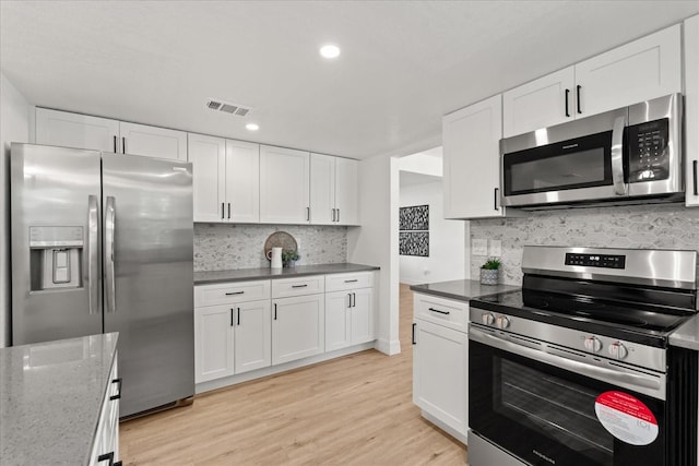 3655 Scott St, Port Orange, FL 32129 - kitchen with stainless steel appliances, white cabinetry, decorative backsplash, light wood-style floors, and dark stone counters