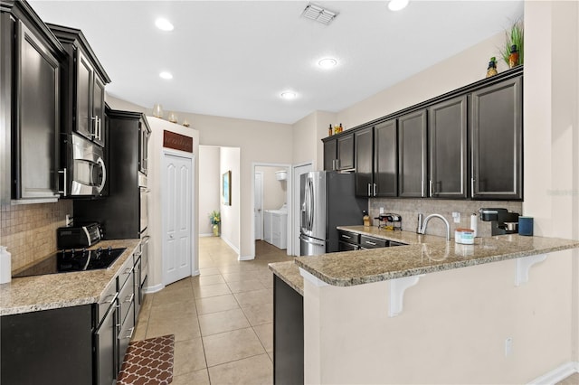 727 Grape Ivy Ln, New Smyrna Beach, FL 32168 - kitchen with appliances with stainless steel finishes, dark cabinets, a breakfast bar area, tasteful backsplash, and recessed lighting