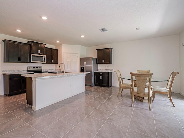 1915 Ganyard Ave SW, Palm Bay, FL 32908 - kitchen featuring stainless steel appliances, light tile patterned floors, recessed lighting, dark brown cabinets, and a kitchen island with sink