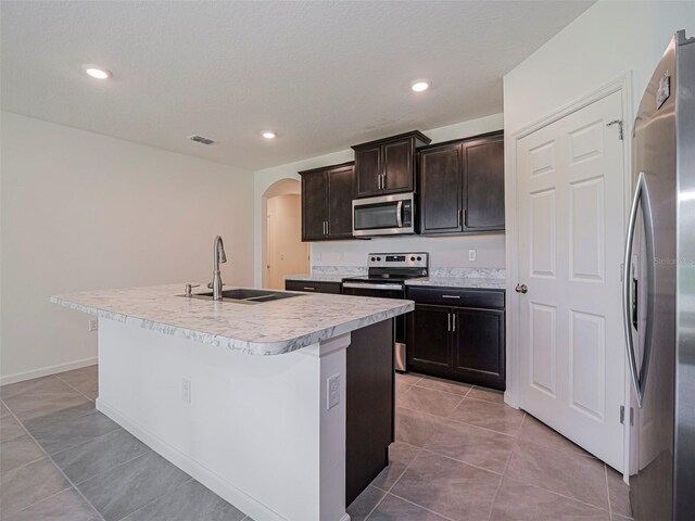 1915 Ganyard Ave SW, Palm Bay, FL 32908 - kitchen with stainless steel appliances, arched walkways, a kitchen island with sink, light countertops, and light tile patterned flooring